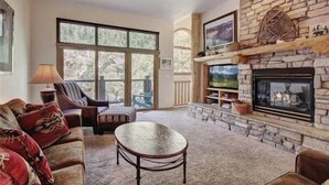 A living room with a stone fireplace, large windows, and a cozy seating area. - Northstar Townhomes in Keystone 2 Bedroom Rental (Keystone)