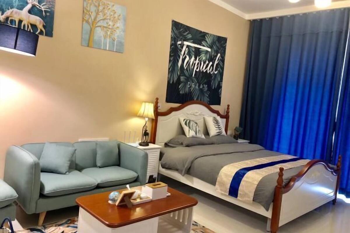 A hotel room with a bed, a sofa, a bedside table, and a lamp.
