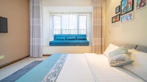 Un dormitorio con cama, un asiento junto a la ventana, cortinas e imágenes enmarcadas en la pared.