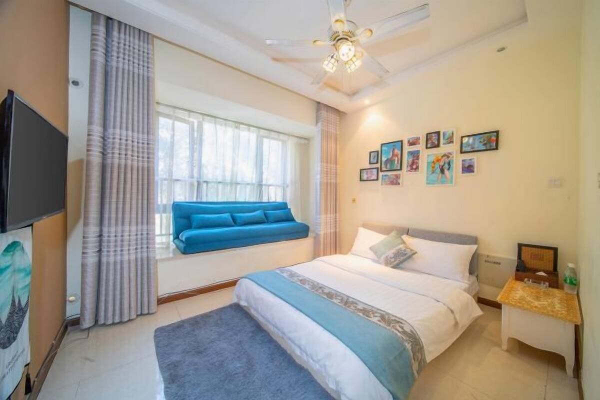 A bedroom with a bed, a window with curtains, a ceiling fan, and wall art.