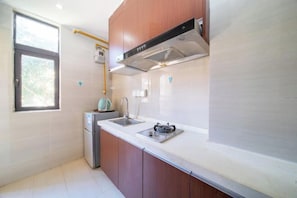 A compact kitchen with a built-in stove, a sink, and a window. - Yijiayi Holiday Hotel (Jinghong)