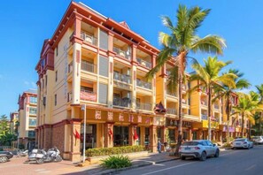 A multi-story hotel with balconies, palm trees, and parked cars. - Yijiayi Holiday Hotel (Jinghong)