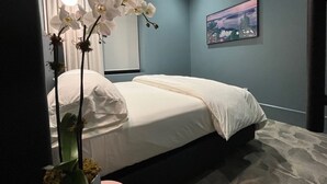 Una camera da letto con un letto, una finestra con tende, un quadro appeso al muro e un vaso con fiori.