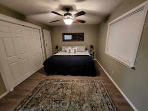 A bedroom with a bed, a ceiling fan, a window with blinds, and a door. - Spacious Family Farmhouse (Pikeville)