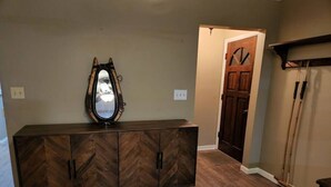 Un mueble de madera con patrón de espiga, un espejo, una puerta y una escoba apoyada en la pared.