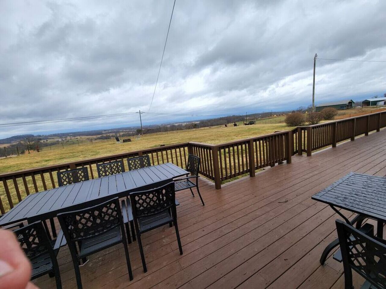 A wooden deck with outdoor seating, a view of a grassy field, and a cloudy sky.