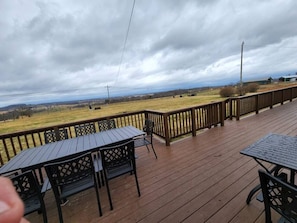 A wooden deck with outdoor seating, a view of a grassy field, and a cloudy sky. - Spacious Family Farmhouse (Pikeville)