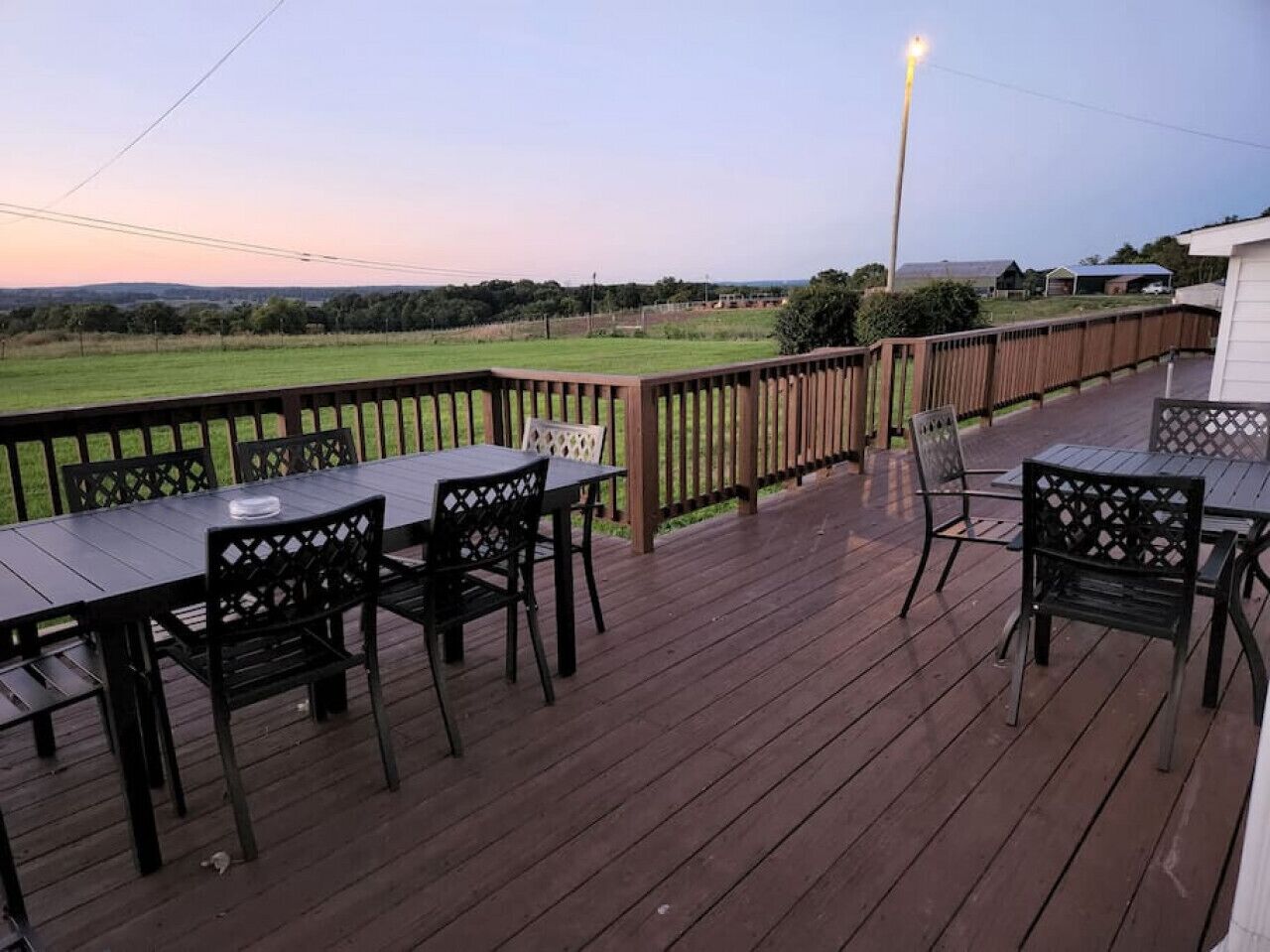 Eine Holzterrasse mit Gartenmöbeln, ein Holzzaun und Blick auf ein grünes Feld.