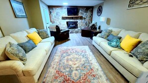 Una sala de estar con dos sofás, un tapete, una pared de piedra, una chimenea y un televisor.