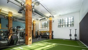 Un gimnasio con suelo de césped artificial, equipamiento de ejercicio y ventanas amplias.