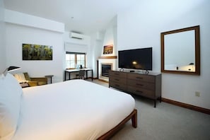 Ein Hotelzimmer mit einem großen Bett, einem Fernseher, einem Schminktisch, einem Schreibtisch und einem Kamin.