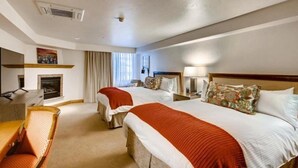 A hotel room with two beds, a desk, a chair, a fireplace, and a window with curtains. - Vail Village Hotel Room With 2 Queens (Vail)