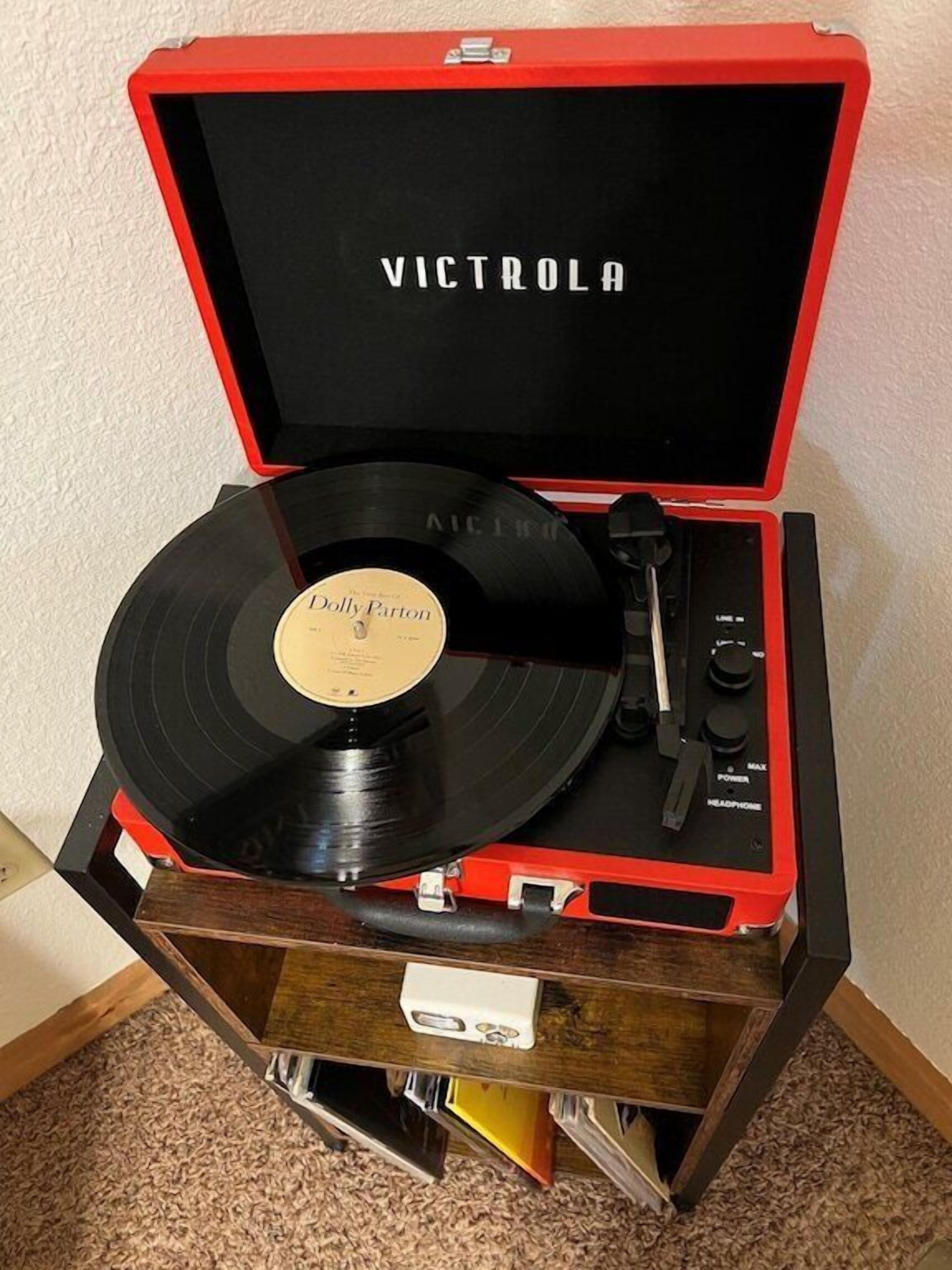 Un tocadiscos Victrola rojo con un disco de vinilo titulado 'Dolly Parton' sobre un mueble de madera.