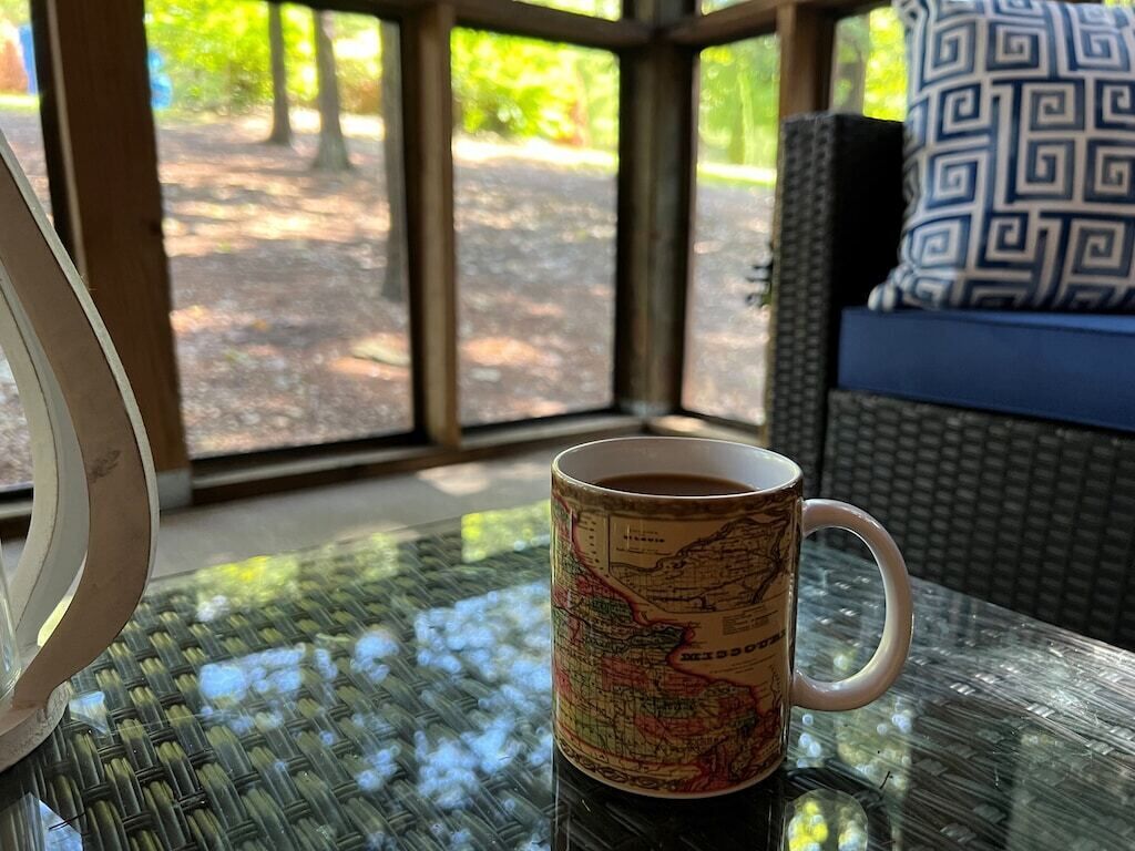 Une tasse à café ornée d’un motif de carte géographique, posée sur une table en verre dans une pièce donnant sur un jardin.