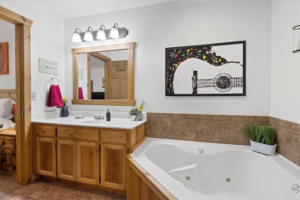 A bathroom with wooden cabinets, a large mirror, a sink, a bathtub, and a framed artwork of a guitar.