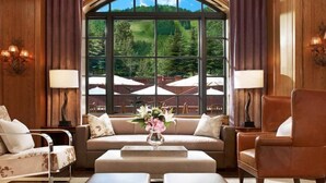 A spacious room with a large arched window offering a view of a green landscape and outdoor seating. - Aspen St Regis Resort Hotel Room With 2 Queens (Aspen)