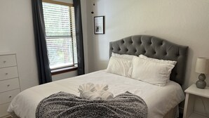 Ein ordentlich bezogenes Bett mit grauem Kopfteil, weißen Kissen und einer grauen und weißen Zudecke mit Muster.
