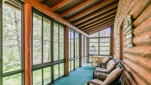 A log cabin with large windows, wicker furniture, and a view of the forest.