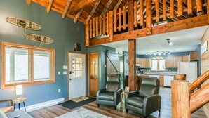A spacious living room with a high ceiling, wooden beams, and a view of the kitchen.