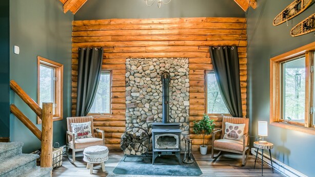 A cozy cabin interior with a stone fireplace, wooden walls, and a log-burning stove.