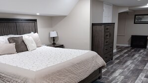 A bedroom with a large bed, a nightstand, a dresser, and a door. - Spacious and Serene Basement (McMinnville)