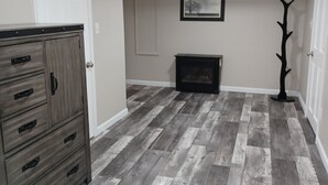 A spacious room with a herringbone-patterned wooden floor, a built-in wooden cabinet, a fireplace, and a framed picture on the wall. - Spacious and Serene Basement (McMinnville)