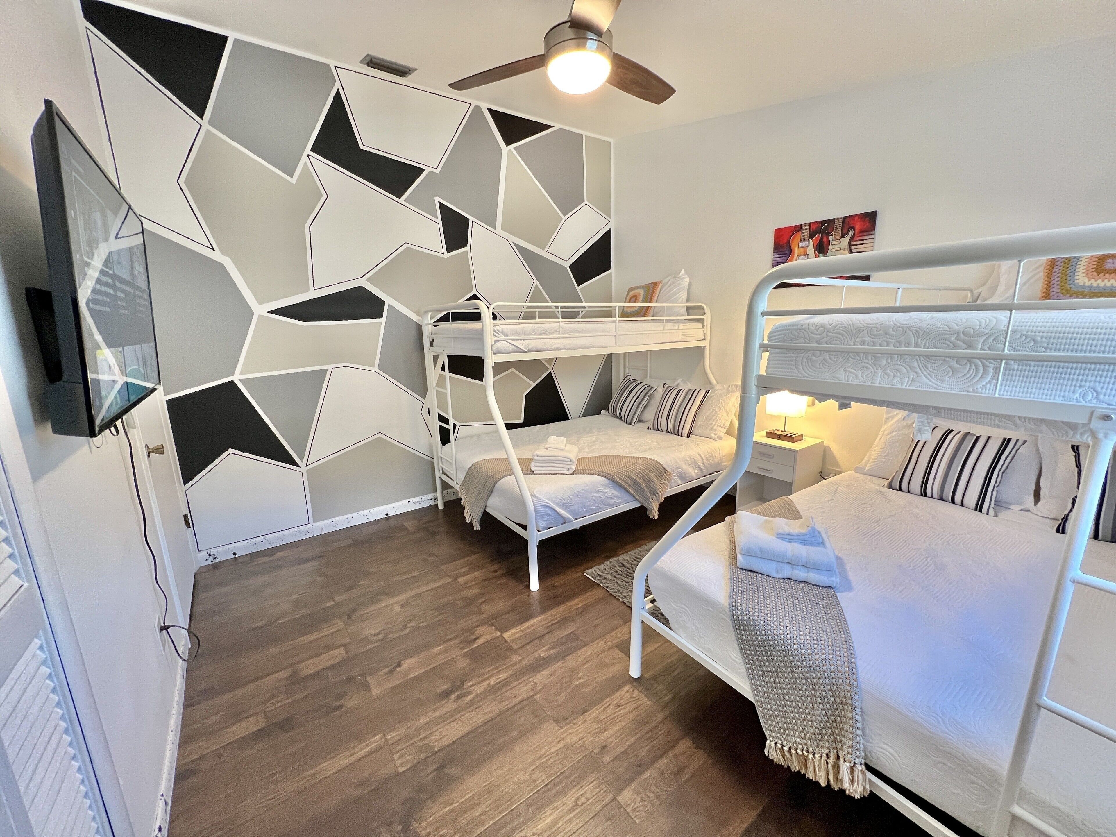 Una habitación con literas, ventilador de techo y pared con diseño geométrico.