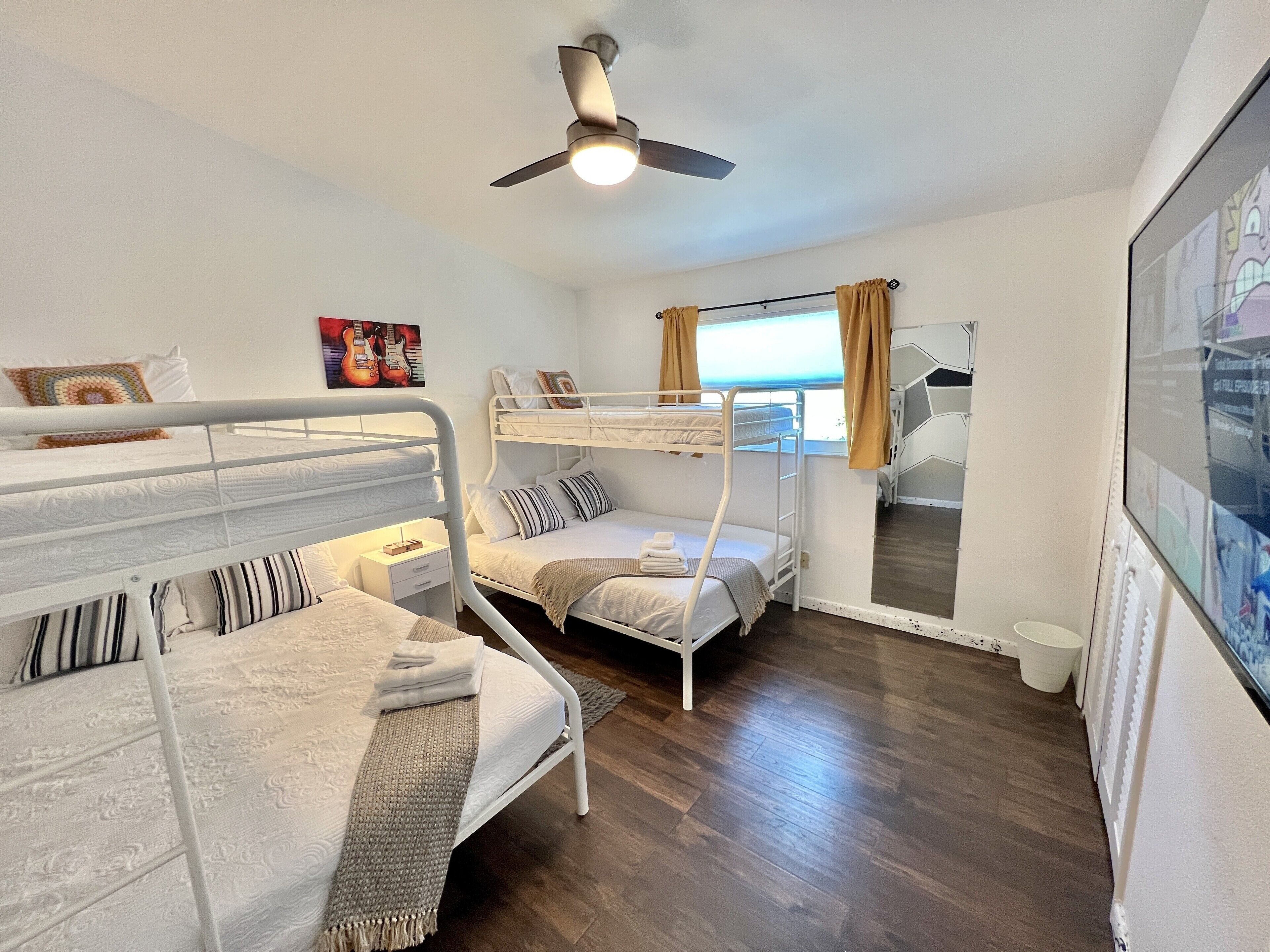 A room with bunk beds, a ceiling fan, a window with curtains, and a poster on the wall.