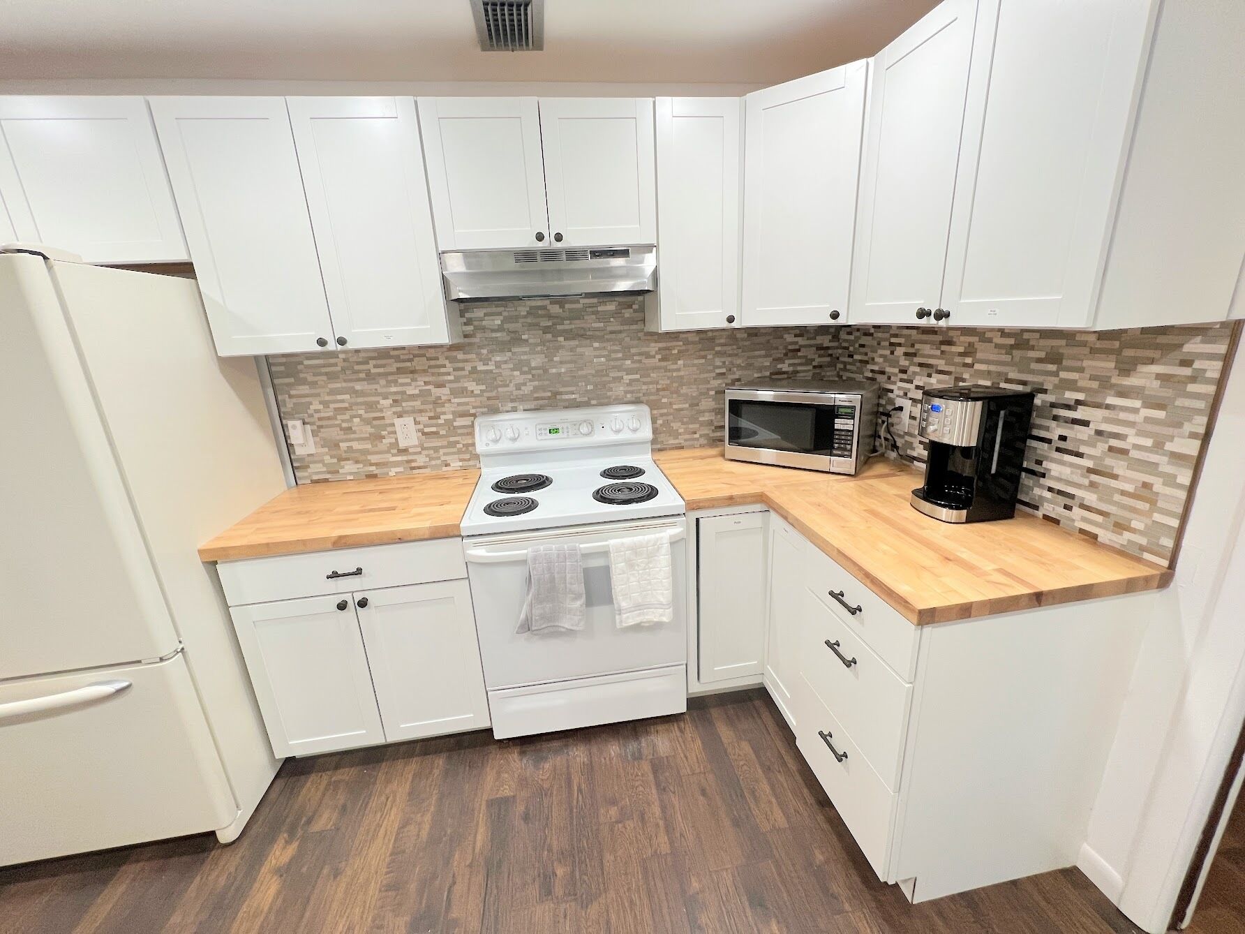 A kitchen with white cabinets, a white stove, a microwave, and a coffee maker.