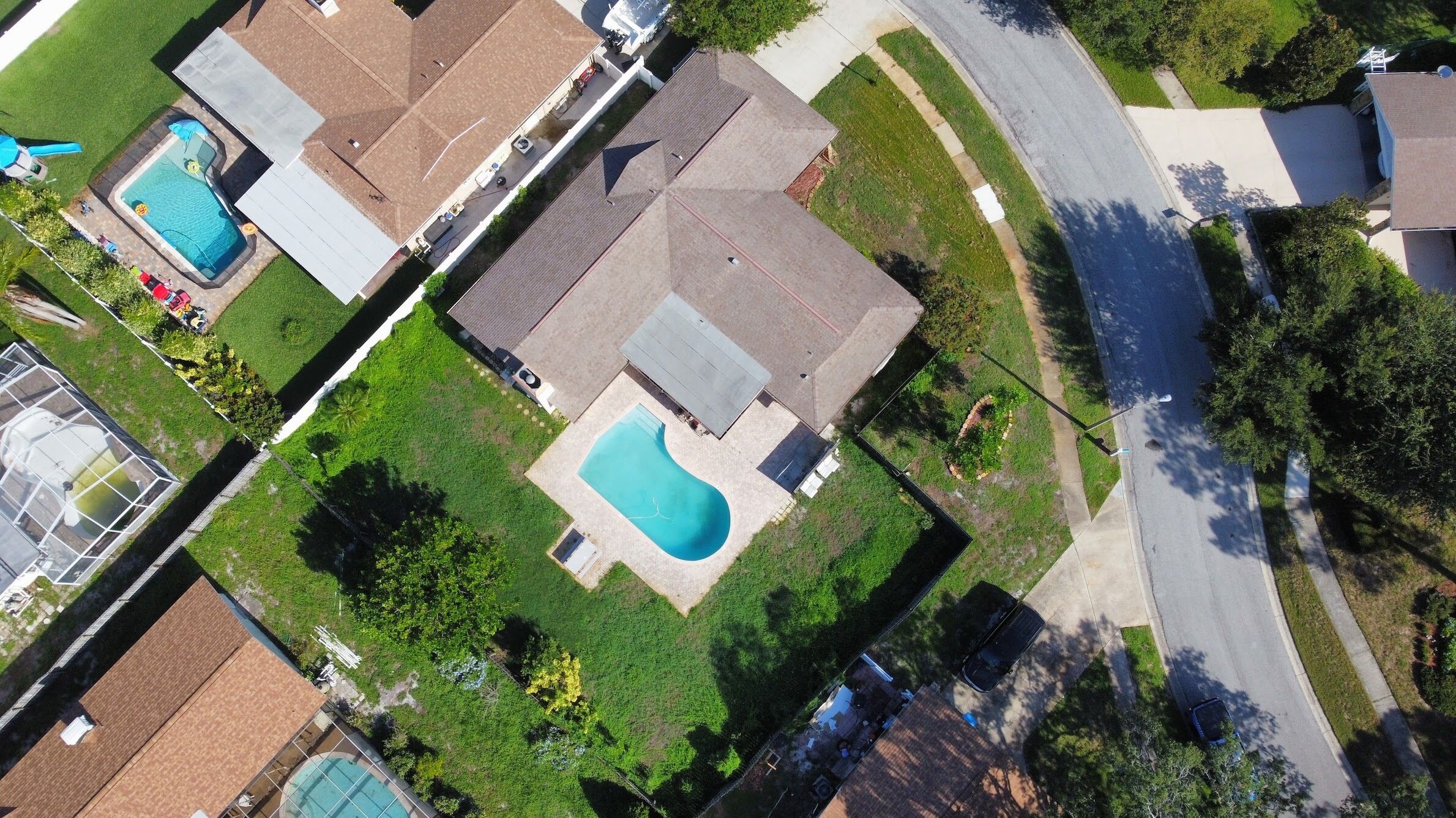 A residential area with a large swimming pool, a tennis court, and a well-maintained lawn.