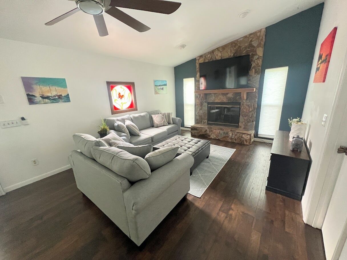 Una sala de estar con un sofá seccional gris, una chimenea y una pared de acento de piedra.