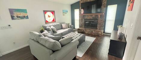 Una sala de estar con un sofá seccional gris, una chimenea y una pared de acento de piedra.