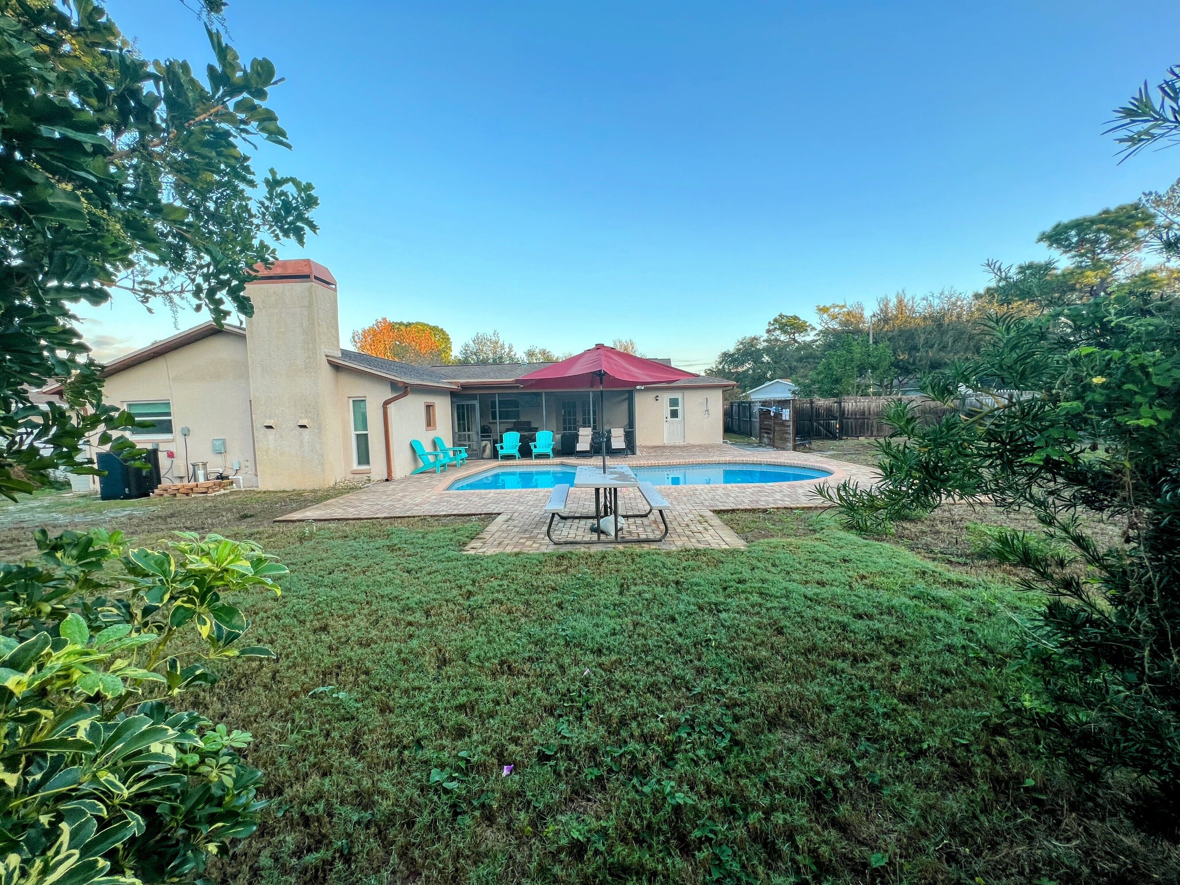 A residential backyard with a swimming pool, patio furniture, and a covered outdoor seating area.