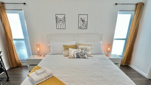 A neatly made bed with a white comforter and a mustard throw blanket, flanked by two bedside tables with lamps.