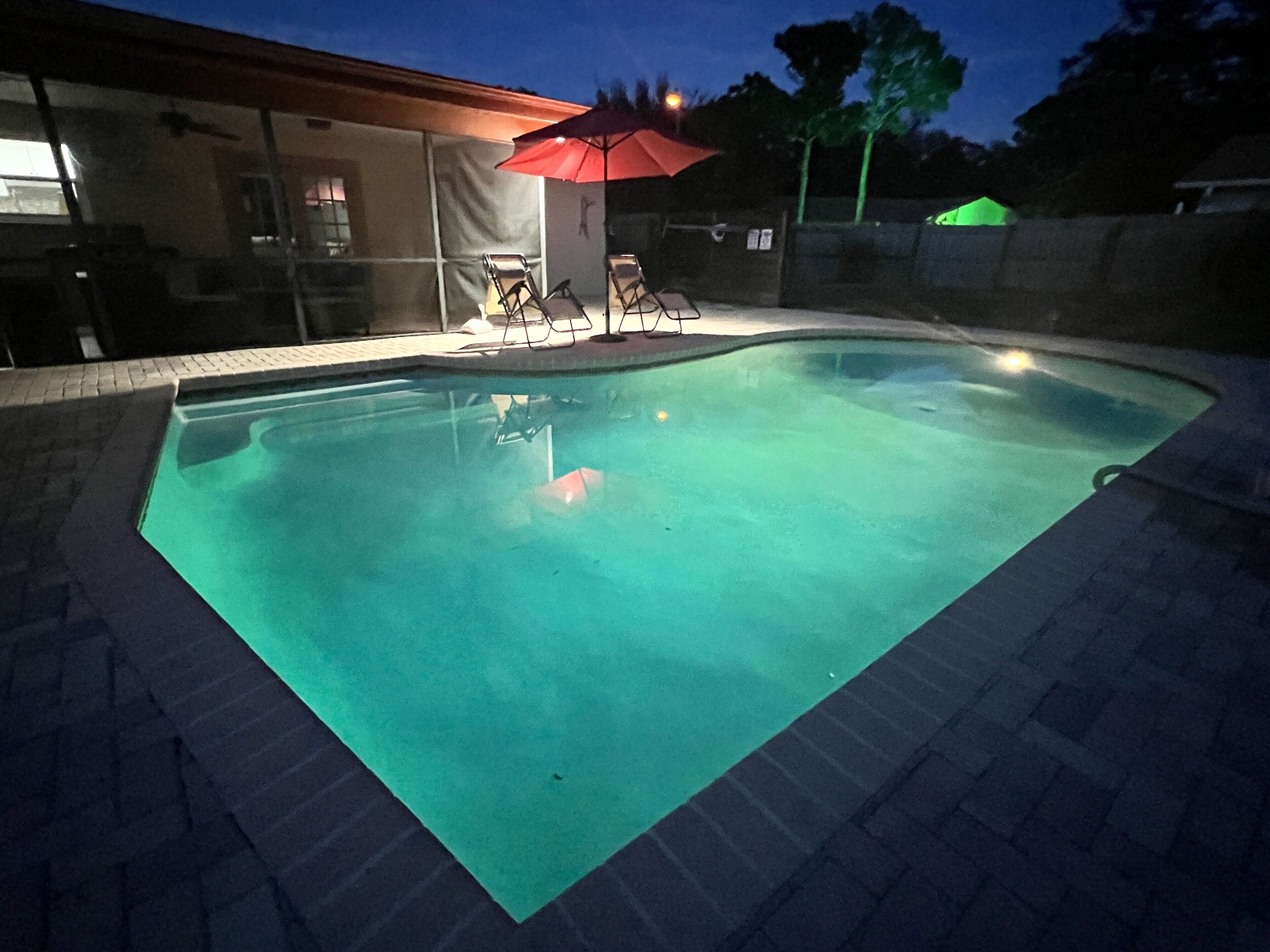 Una piscina con un paraguas rojo, rodeada por un patio de ladrillo.