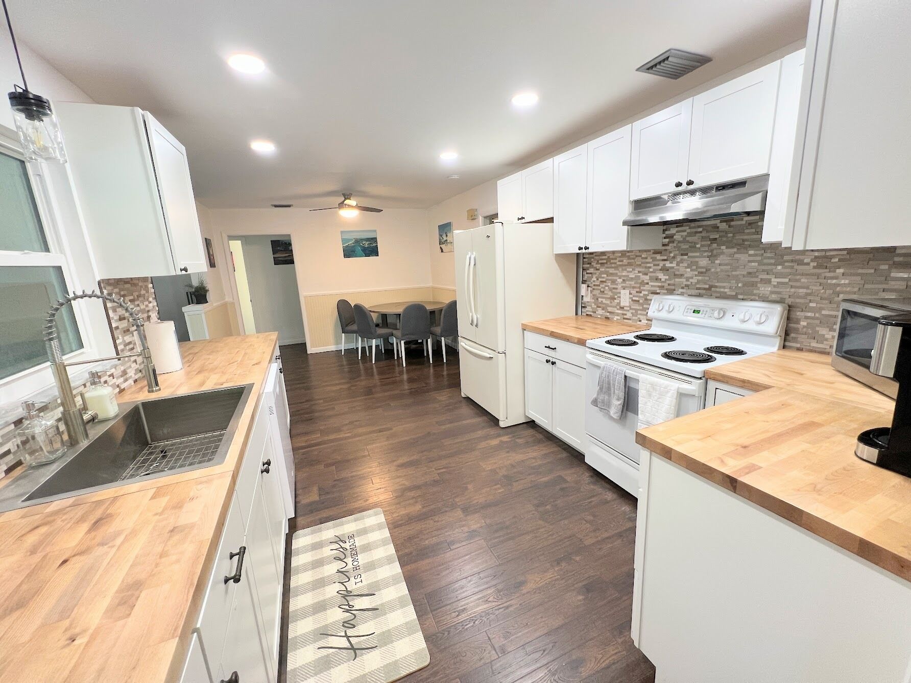 A modern kitchen with white cabinets, a wooden countertop, a stove, and a dining area with chairs.