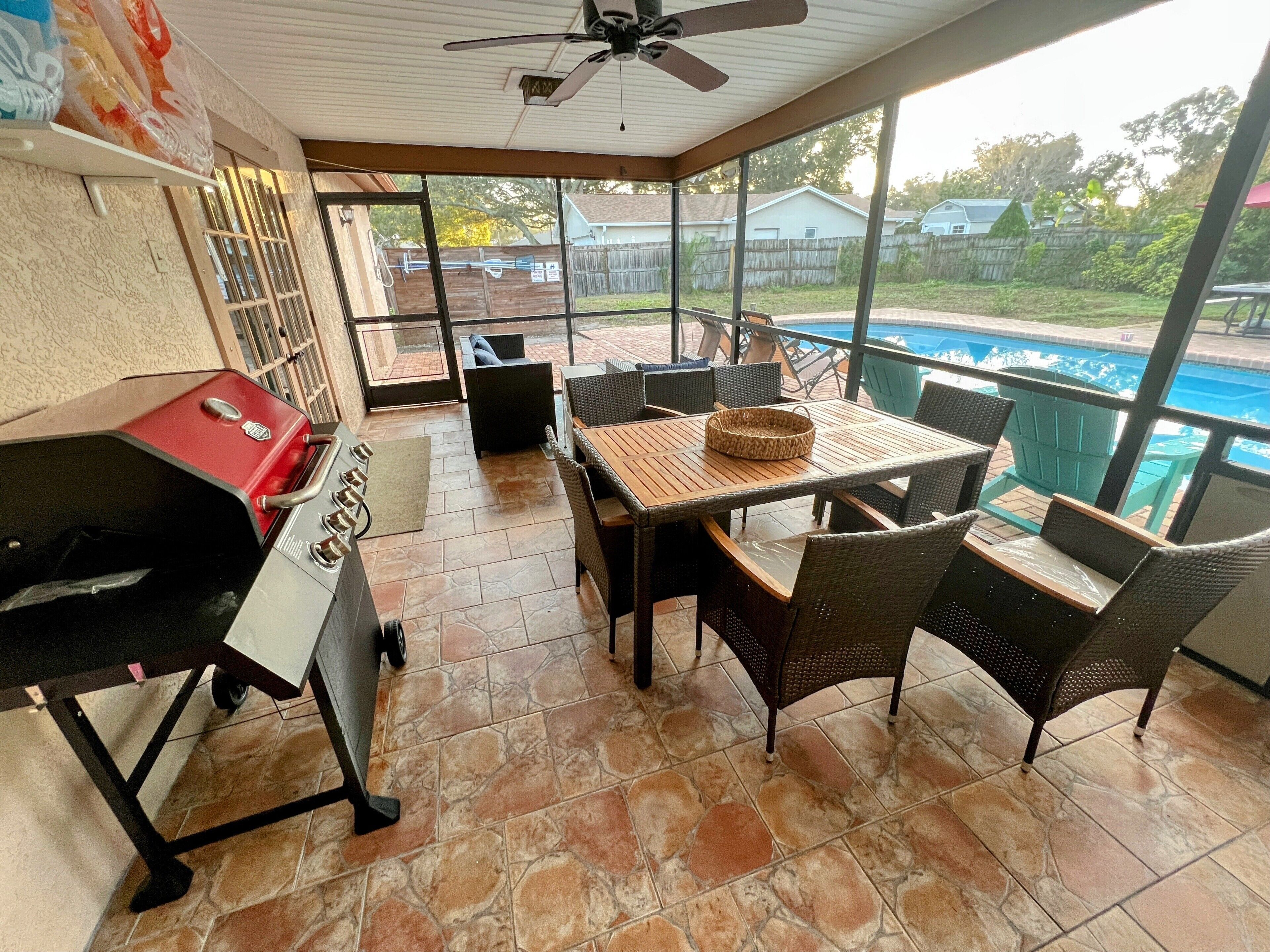 Un patio techado con una parrilla de barbacoa, una mesa de comedor y sillas, con vista a una piscina.