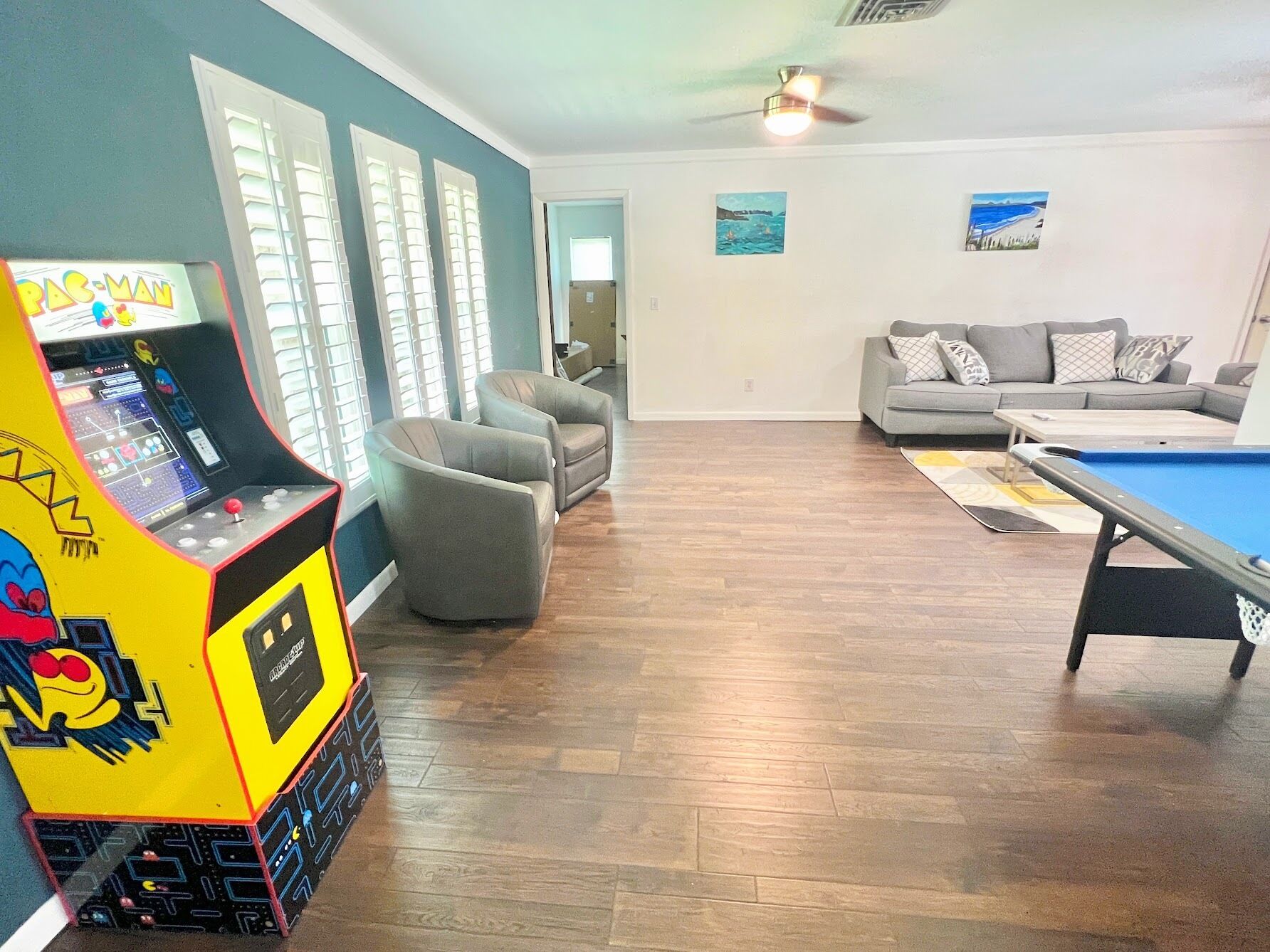 A living room with a pool table, two armchairs, a sofa, and a Pac-Man arcade machine.