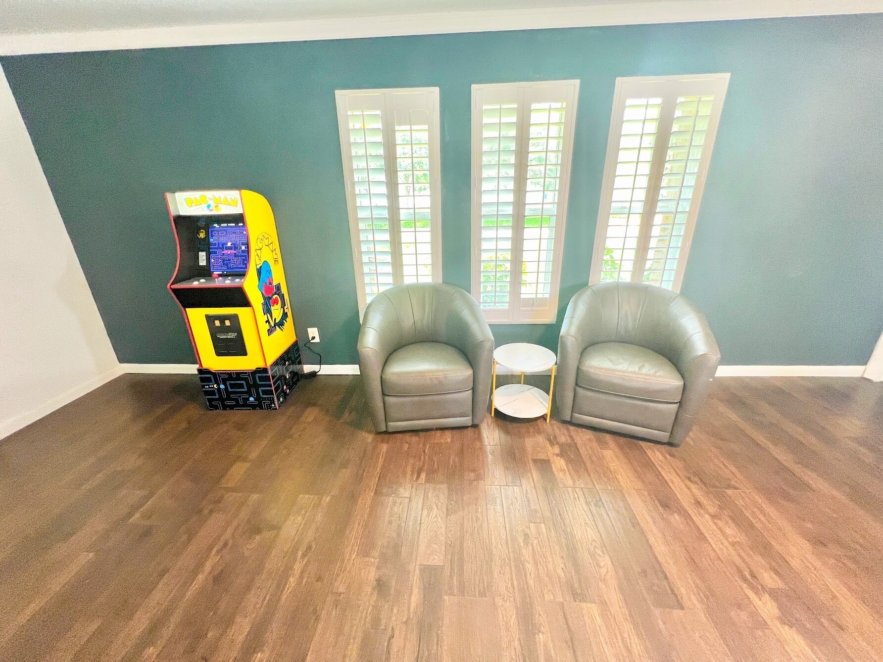 Een kamer met turquoise wanden, twee grijze fauteuils, een witte bijzettafeltje en een gele speelautomaat.