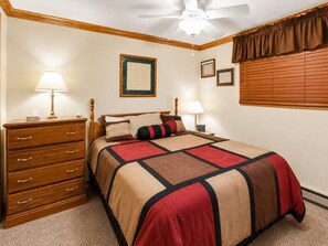 A bedroom with a bed, dresser, ceiling fan, framed pictures, and window blinds.