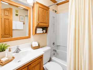A bathroom with a wooden vanity, a white sink, a bathtub, and a shower curtain.
