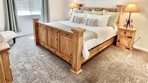 Ein Schlafzimmer mit einem hölzernen Bett, zwei Nachttischen, einem Fenster mit Vorhängen und Wandbildern.