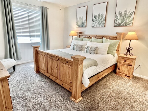 A bedroom with a wooden bed, two bedside tables, a window with curtains, and wall art. - ⭐️Enjoy Las Cruces at this Colorful Rustic Home 3BR (Las Cruces)