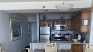 Un comedor con una mesa redonda de vidrio y sillas de mimbre, una cocina con armarios de madera y electrodomésticos de acero inoxidable, y un ventilador de techo.