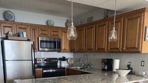 Una cocina moderna con armarios de madera, electrodomésticos de acero inoxidable, encimera de granito y taburetes de bar.