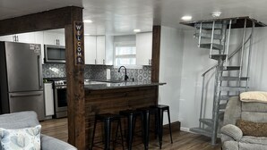 A modern kitchen with a central island, bar stools, and a staircase leading to an upper level.