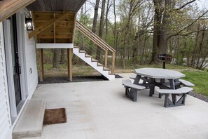 Un espace extérieur abrité doté d’une terrasse en béton, d’un escalier en bois et d’une table de pique-nique avec des bancs.