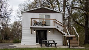 A two-story cabin with a balcony, a staircase, and a picnic table.