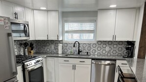 A modern kitchen with white cabinets, a stainless steel range, a dishwasher, and a wooden floor.