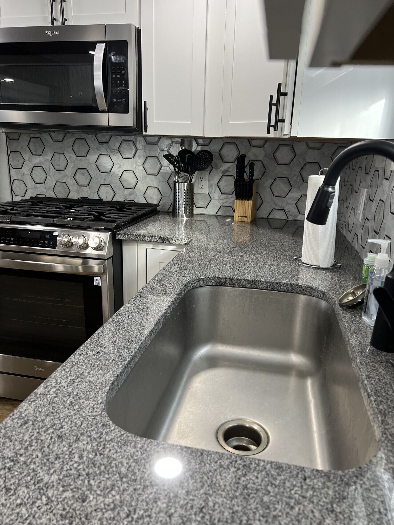 A kitchen with a stainless steel sink, a microwave, a stove, and a paper towel dispenser.
